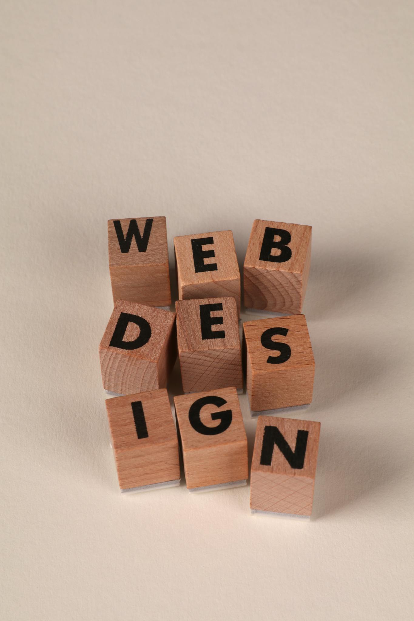 Wooden letter blocks arranged vertically and horizontally spell out the words "WEB DESIGN" on a neutral background.